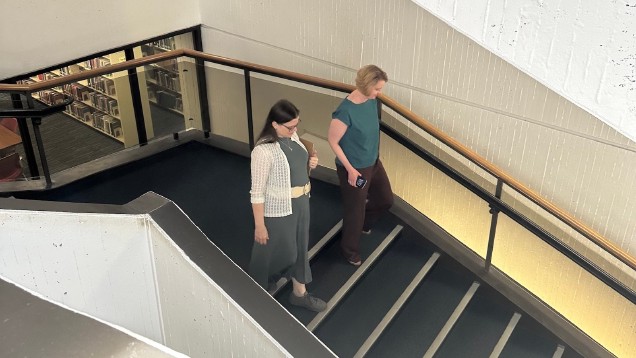two women walking down a flight of stairs with library books in the background