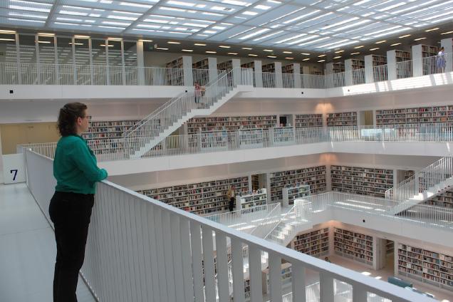 woman standing at a railing looking out over several floors of a modern library with shelves of books